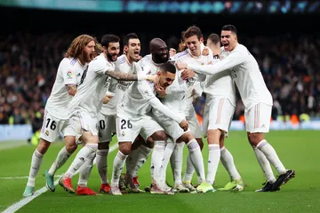 A woman smiling by bright slot machines showing lucky symbols, showcasing the exciting slot offerings at REAL MADRID.